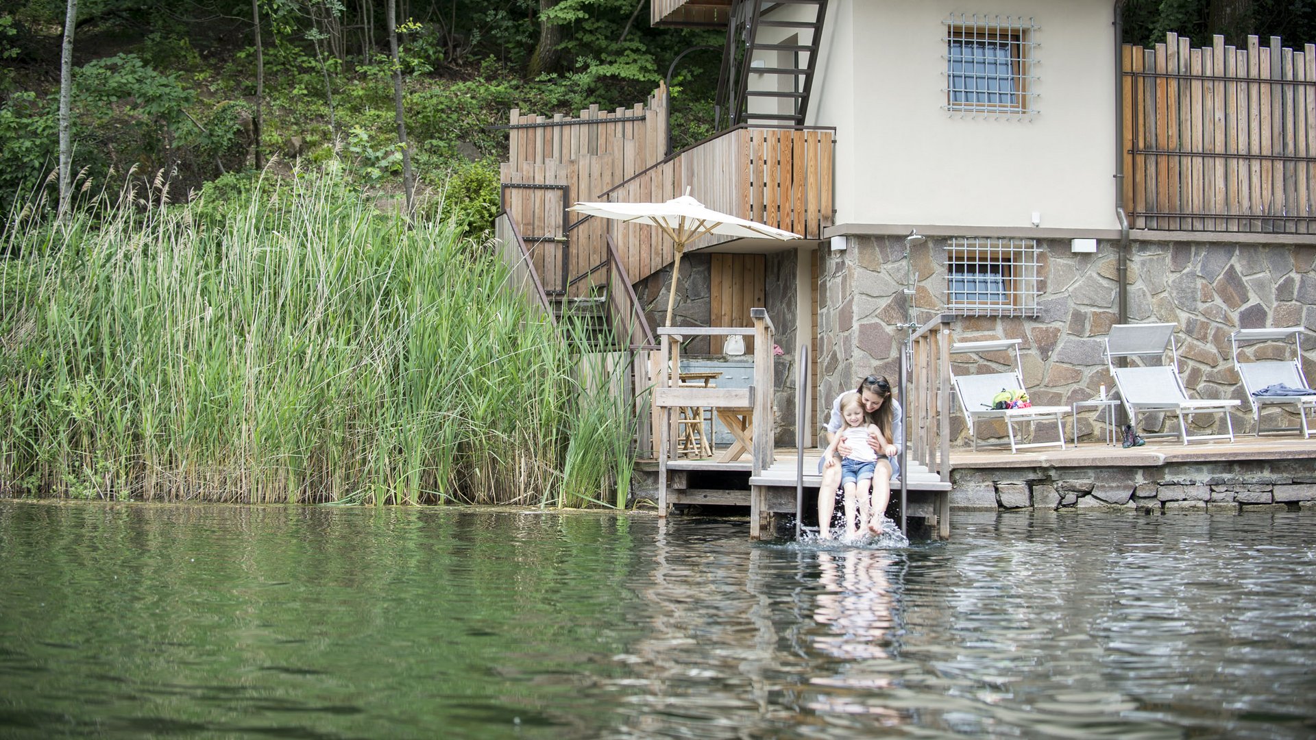 Lakeside wellness holiday: Gartenhotel Moser Woman and child sitting on dock by house at lake splashing water with feet