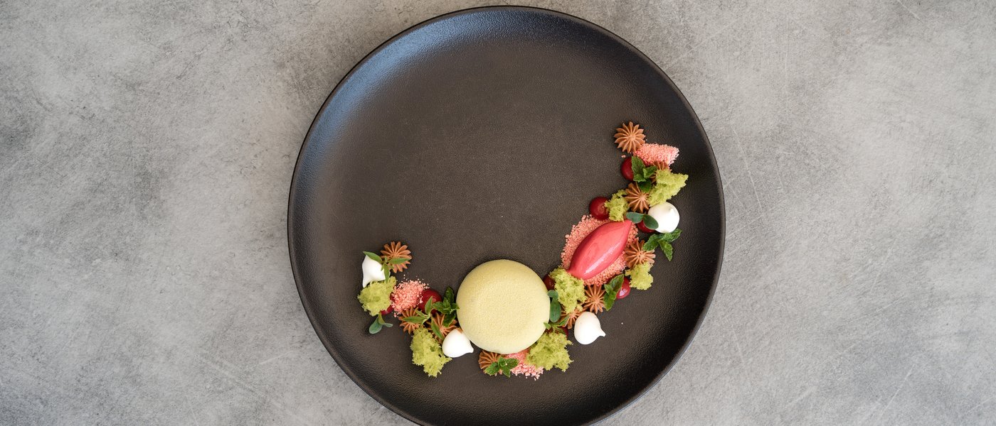 Wellnesshotel mit Gourmetküche: Gartenhotel Moser Kunstvoll angerichtetes Dessert mit grünem Baiser und rotem Sorbet auf schwarzem Teller