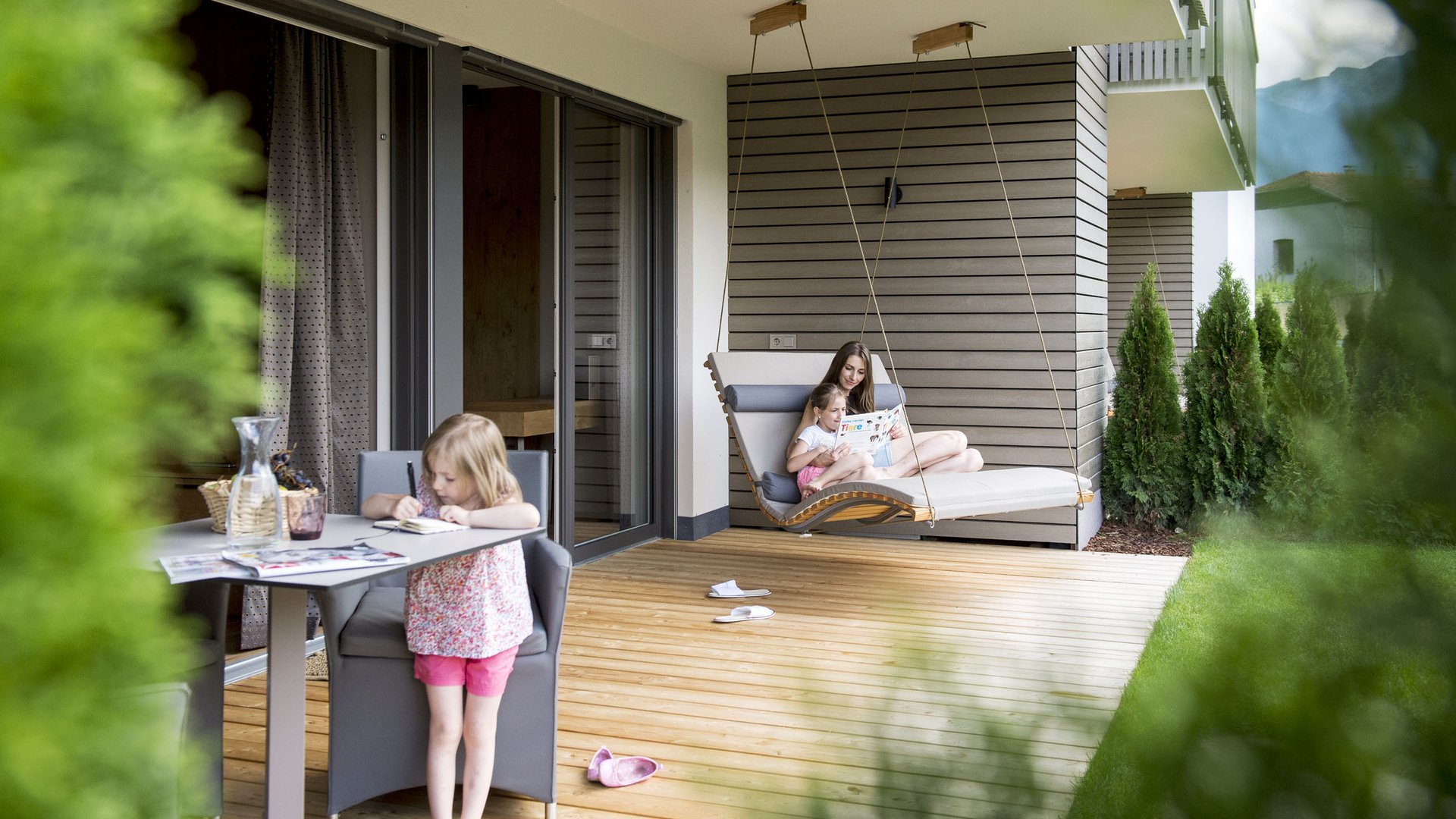 Kinderhotel am See: Gartenhotel Moser Kind malt am Tisch auf Terrasse, Mutter liest Kind auf Hängeliege vor