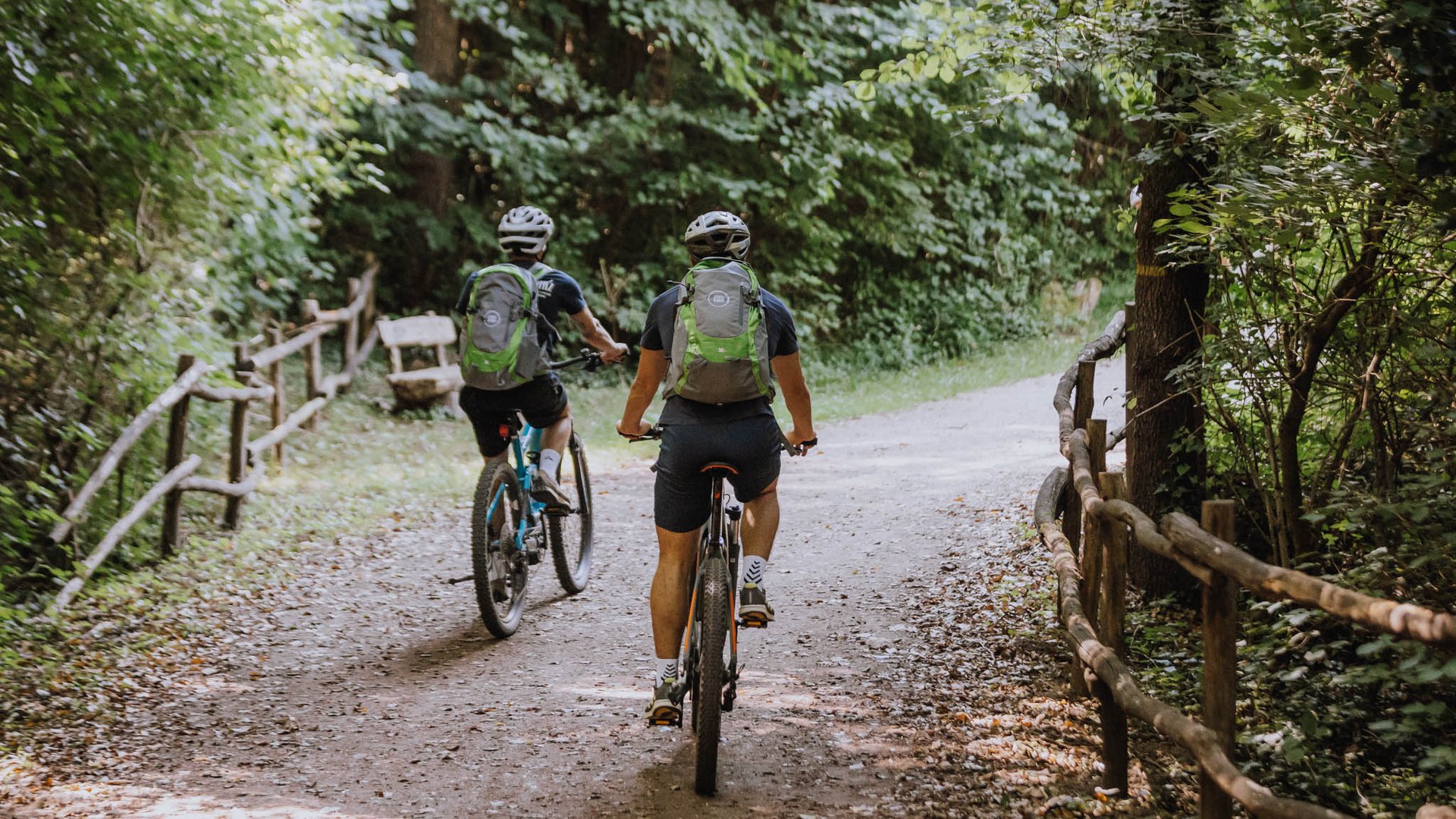 Hotel per famiglie in Trentino-Alto Adige: tour in bici Due ciclisti con casco e zaino pedalano su un sentiero boschivo