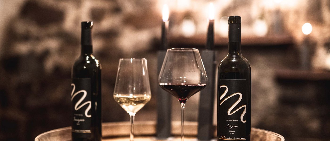 Hotel on the Wine Road in South Tyrol Wine bottles and glasses of red and white wine on a wine barrel with candles in the background