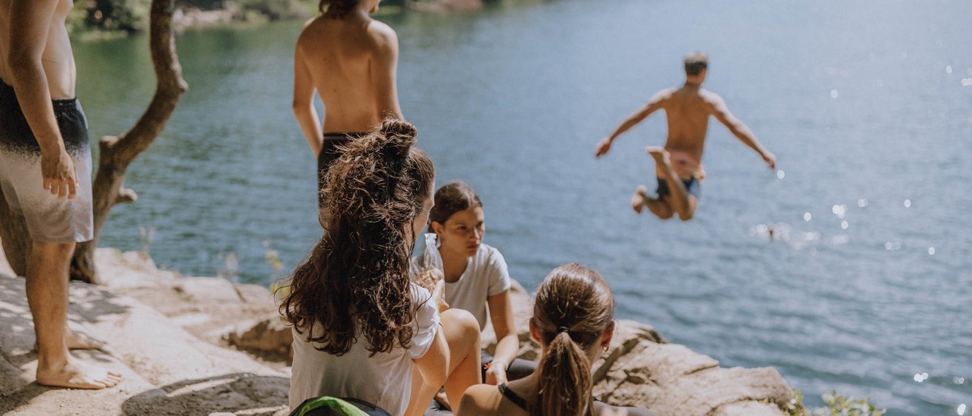 Hotels nahe dem Kalterer See 4-Sterne-Superior Gruppe junger Leute am See, einer springt ins Wasser vom Felsen