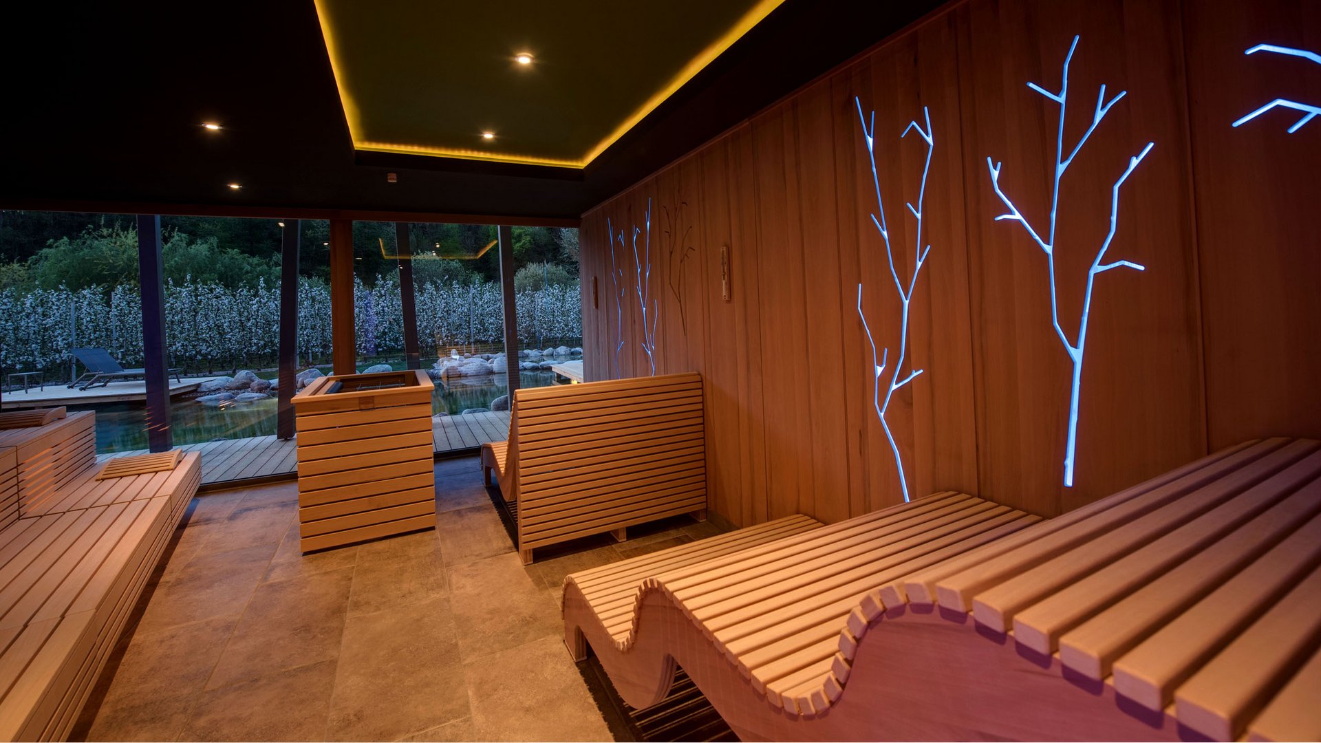Hotel am Montiggler See: Gartenhotel Moser Moderner Saunaraum mit Holzliegen und blauen Baumlichtakzenten