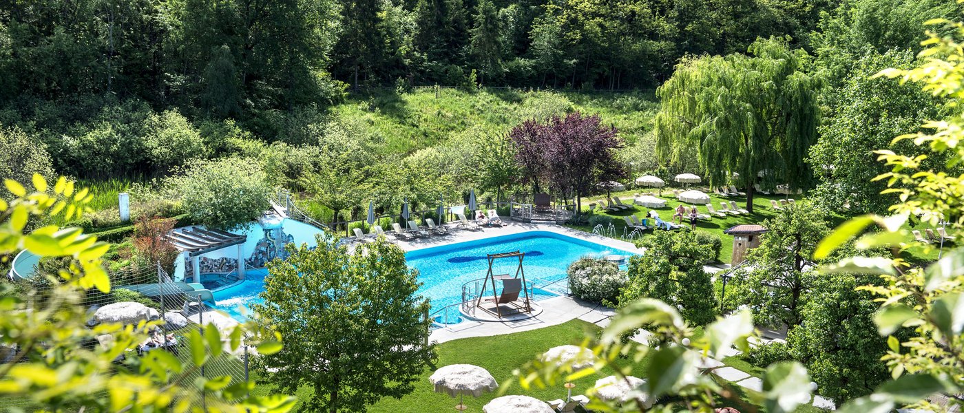 Urlaub in Südtirol im Hotel mit Pool am See Freiluftpool und Grünanlage in einem Waldgebiet bei sonnigem Wetter