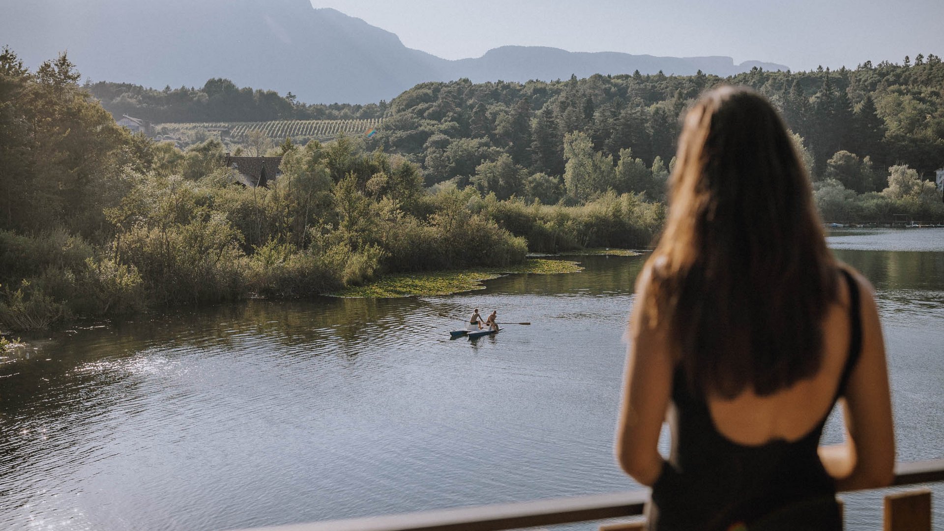 Wellnessurlaub am See: Gartenhotel Moser Frau schaut auf Fluss mit zwei Menschen in Ruderboot vor bewaldeten Hügeln