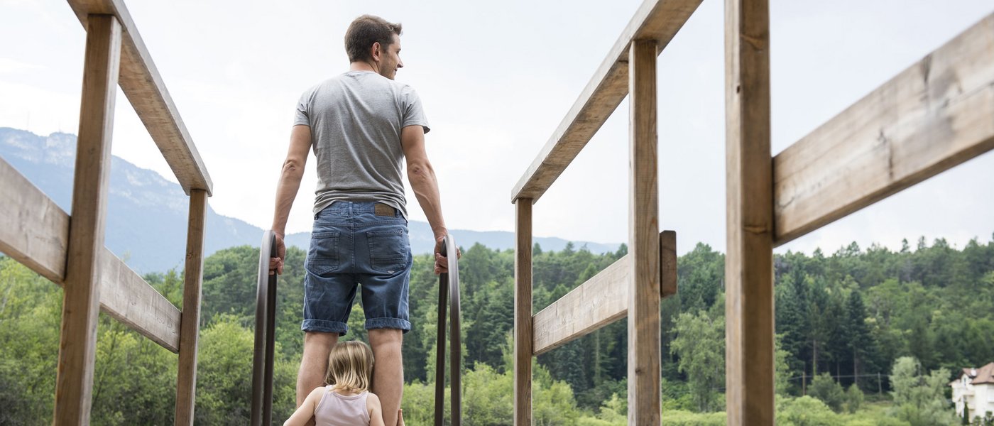 Kinderhotel am See: Gartenhotel Moser Mann und Kind auf Steg am See mit Wald und Bergen im Hintergrund