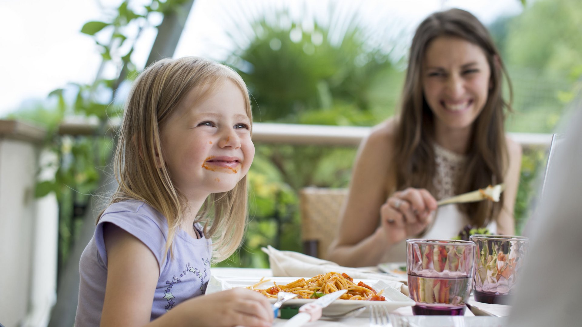 Im Wellnesshotel glutenfrei genießen Lachendes Mädchen mit Spaghetti-soßenflecken beim Essen mit Familie im Freien