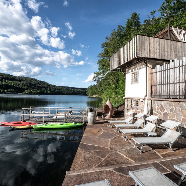 Hotel am Montiggler See: Gartenhotel Moser Seeblick mit Sonnenterrasse und Kajaks am Steg bei bewölktem Himmel