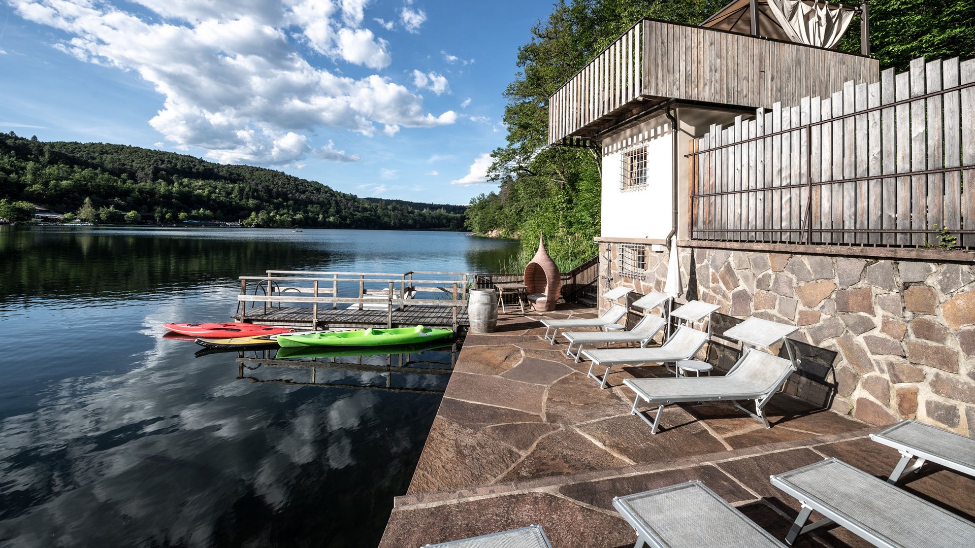 Lakeside wellness holiday: Gartenhotel Moser Lake view with sun terrace and kayaks on the dock under cloudy sky