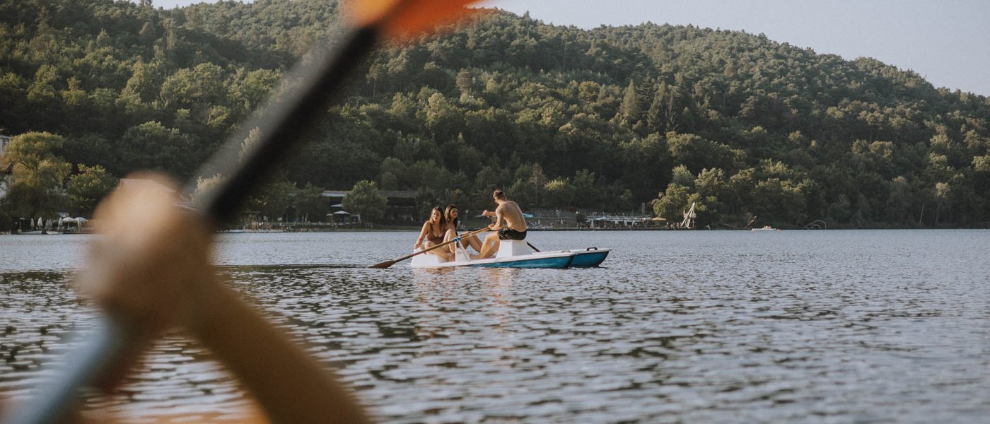 Hotel bei Eppan an der Weinstraße: Gartenhotel Moser Person rudert mit Paddel auf einem See mit Bergblick