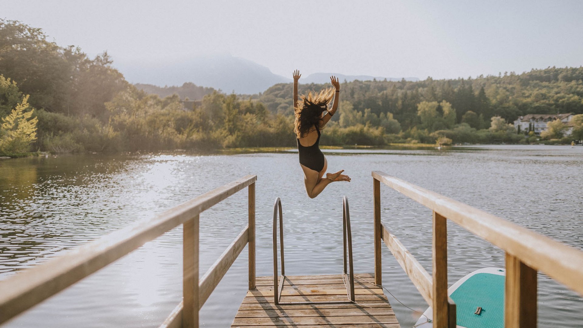 Frau springt von Steg ins Seewasser an einem sonnigen Tag