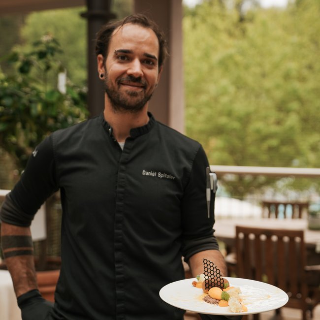 Im Wellnesshotel glutenfrei genießen Koch zeigt elegantes Dessert auf Terrasse mit grüner Landschaft im Hintergrund