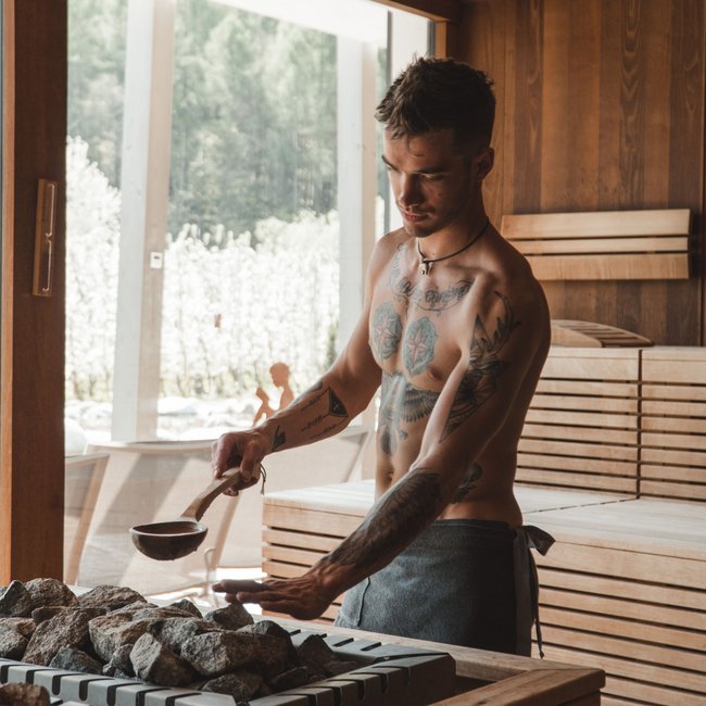 Hotel wellness in Alto Adige per soli adulti Uomo versa acqua sulle pietre della sauna in una stanza di legno