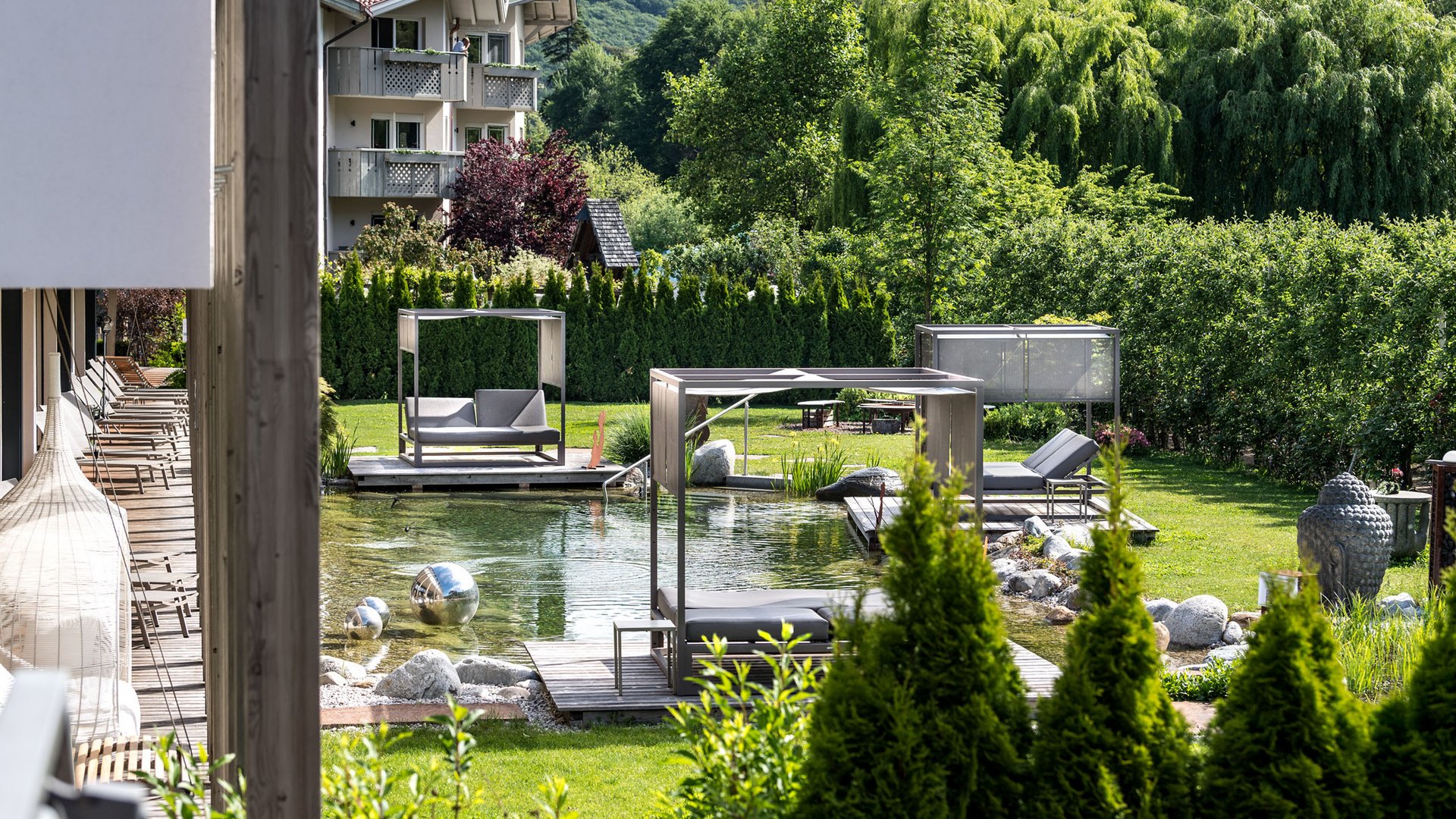 Hotel am Montiggler See: Gartenhotel Moser Moderne Gartenmöbel und Teich vor einem Gebäude in einer grünen Landschaft