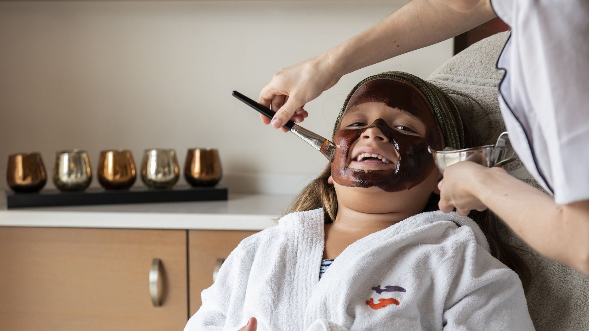 Familienhotel in Südtirol: Gartenhotel Moser Kind bekommt Gesichtsmaske im Spa getragen von Fachkraft