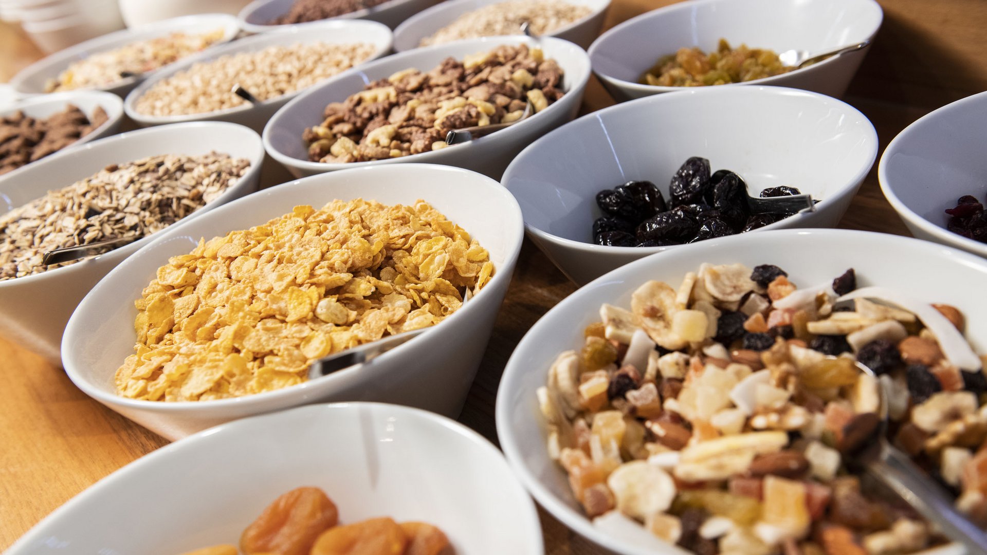 Im Wellnesshotel glutenfrei genießen Verschiedene Müslis und Trockenfrüchte in weißen Schalen auf Holztisch