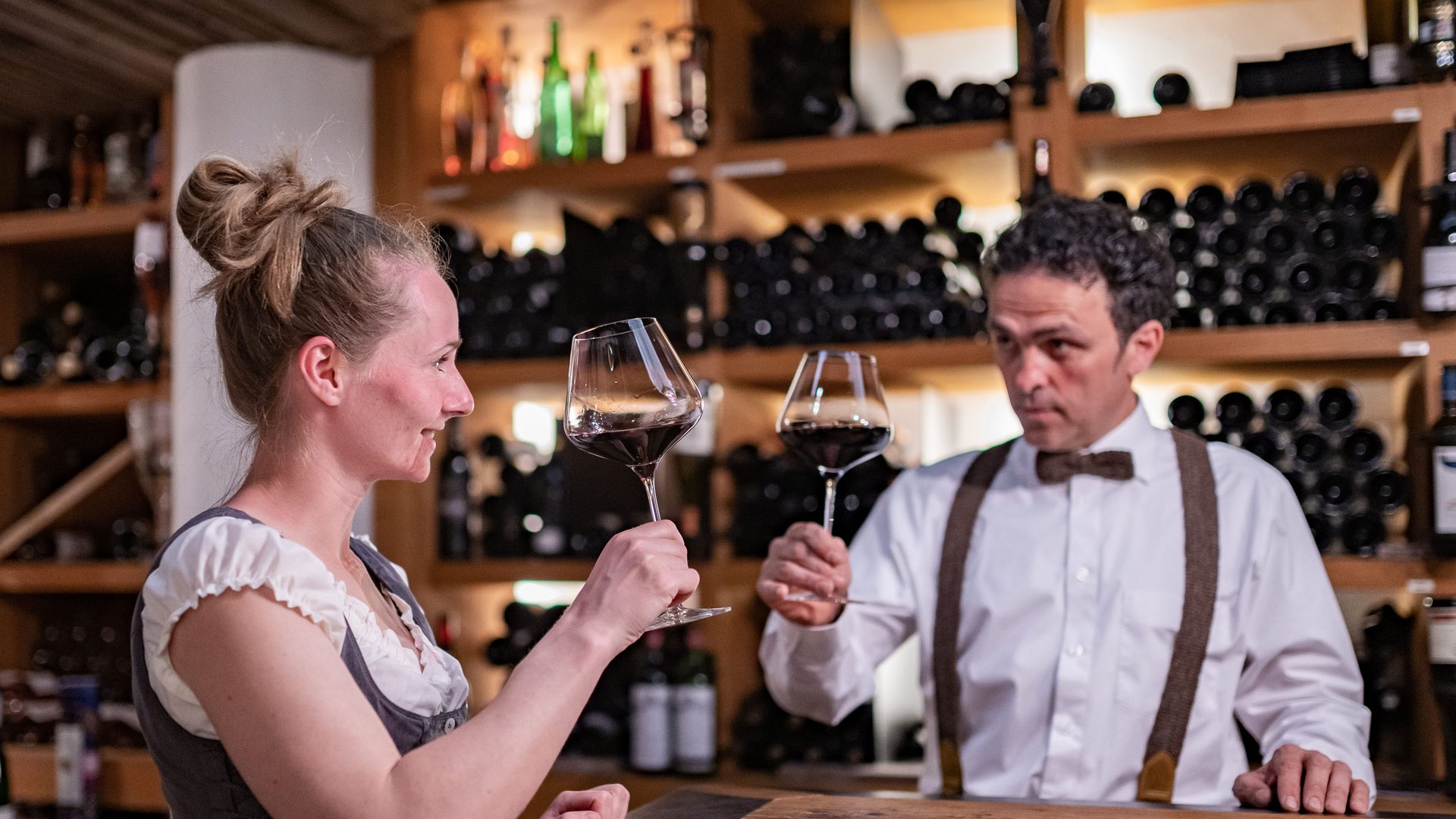 Hotel benessere in Alto Adige: posizioni Donna e uomo brindano con calici di vino rosso in una cantina