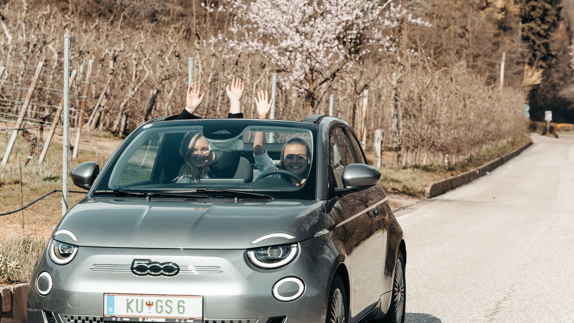 Hotel by the lake in South Tyrol: cabriolet & Vespa Two people waving from a gray Fiat 500 convertible on a country road