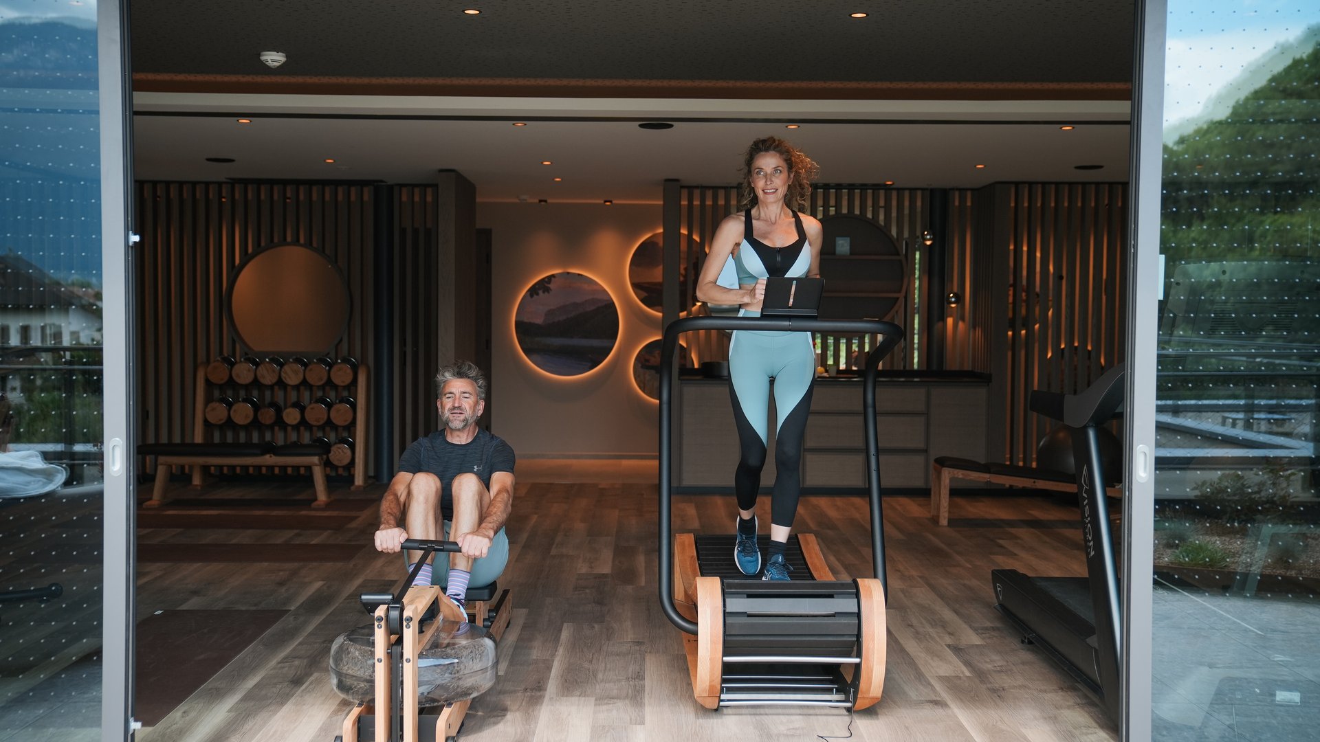 Wellnessurlaub in Südtirol für adults only Mann rudert und Frau läuft auf Geräten im modernen Fitnessraum