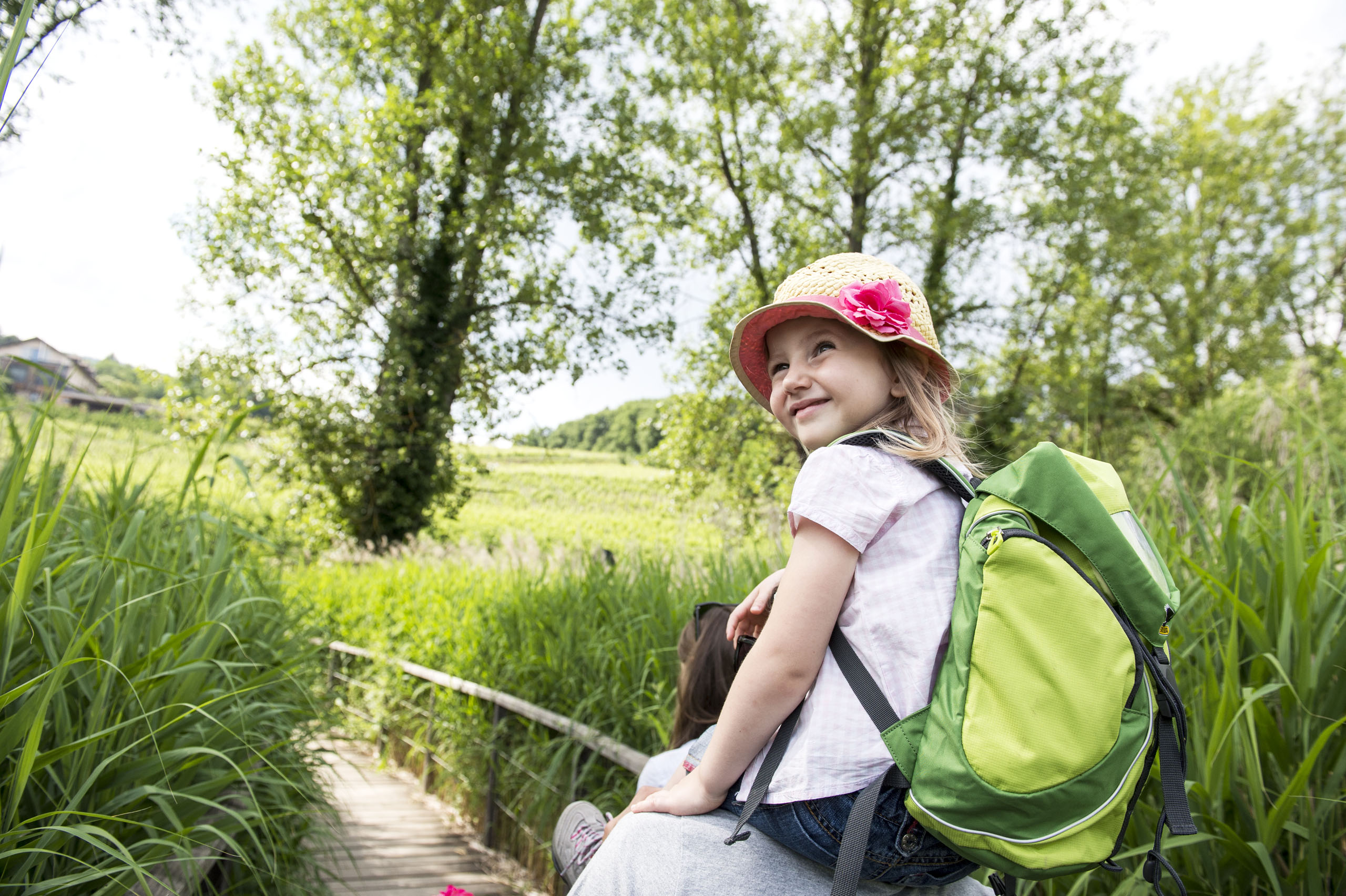 Lago di Caldaro: passeggiata e varie attività nei dintorni del Gartenhotel Moser Bambina con zaino verde in natura sulle spalle di un adulto