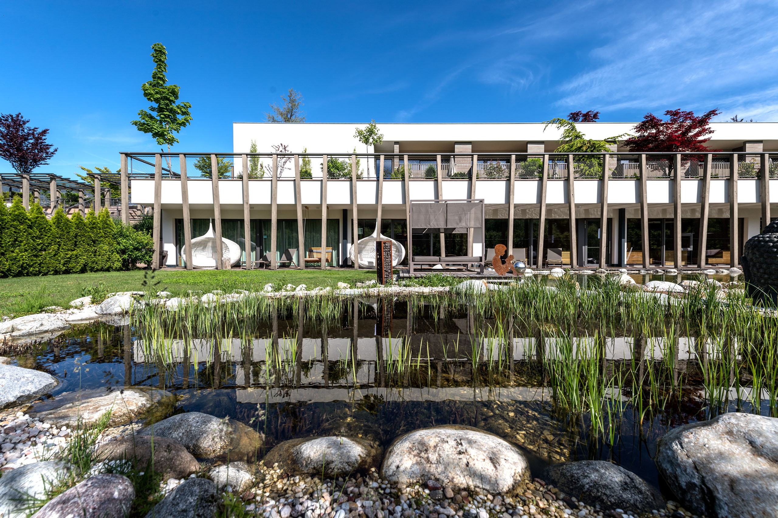 Urlaub in Südtirol im Hotel mit Pool am See Moderne Villa mit großem Teich und Garten bei sonnigem Wetter