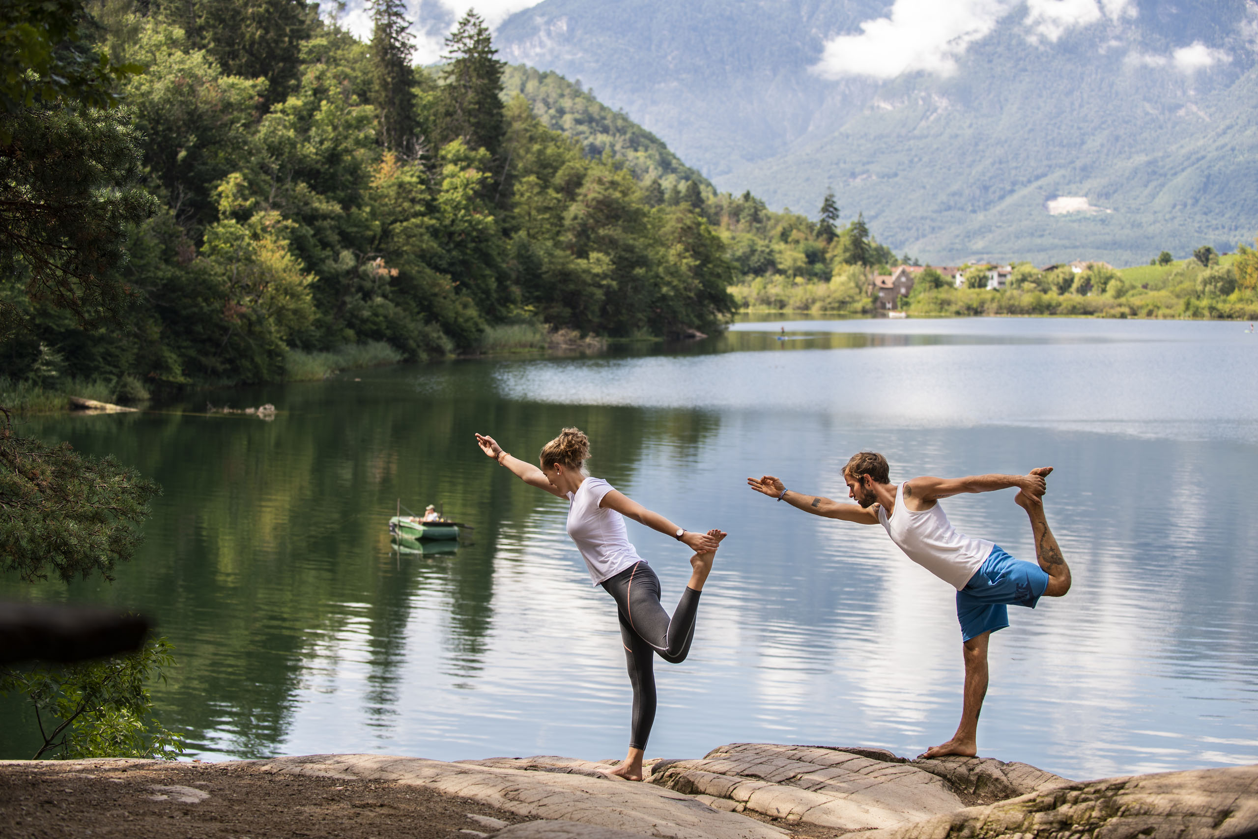 Hotel wellness in Alto Adige per soli adulti Coppia fa yoga sul lago con foresta e montagne sullo sfondo